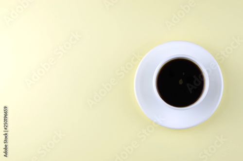 One cup with a saucer with coffee on a light yellow background.