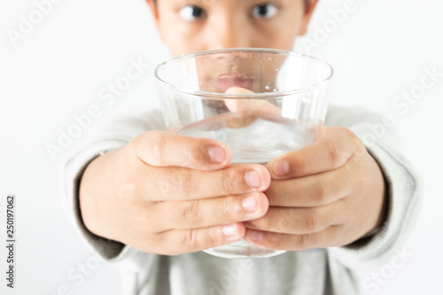 A boy drinking water from glass on white background.