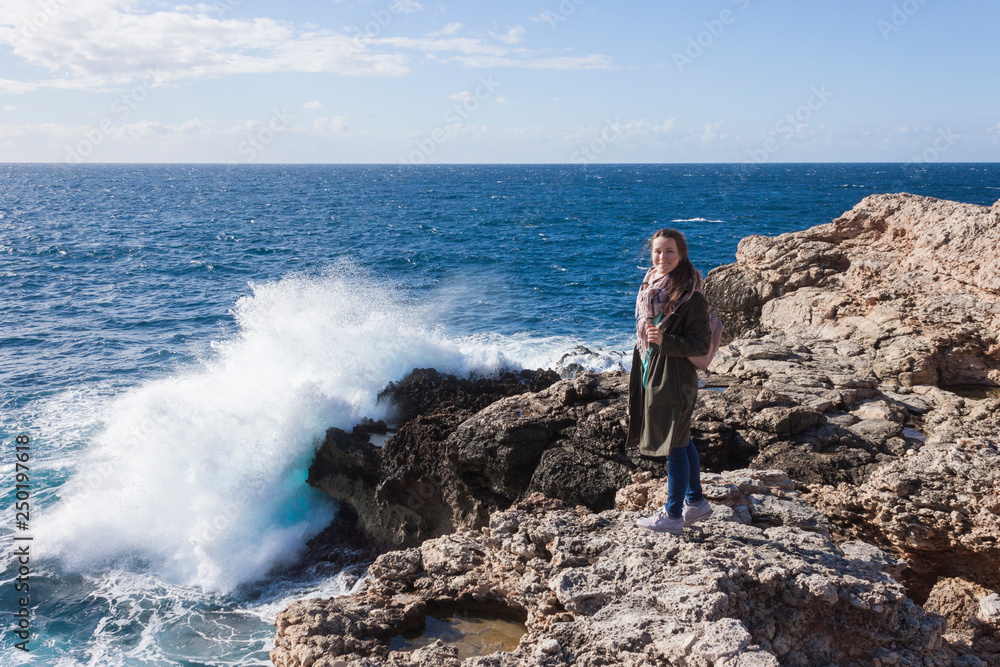 Happy female tourist in coat stand on cliff and enjoys sea view in Malta