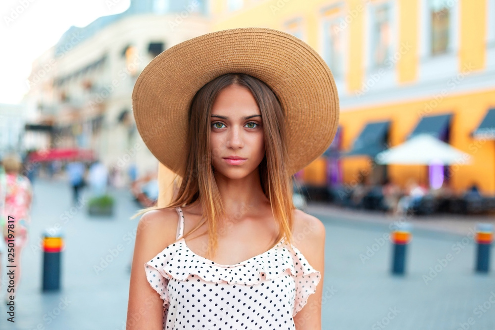 Sunny lifestyle fashion portrait of young stylish hipster woman walking on the street, wearing trendy outfit, straw hat.Beautiful young woman walking in the city. Fashion.Copy space.