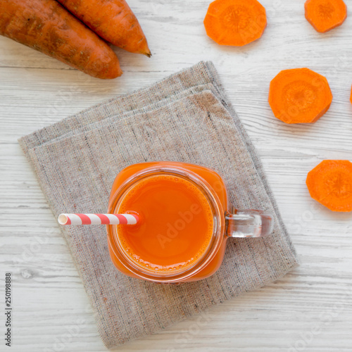 Glass jar of carrot smoothie on a white wooden table, top view. Flat lay, overhead, from above.