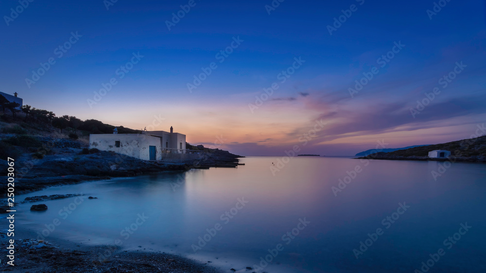 Fototapeta premium Just after sunset with some boathouses in the bay of Limnionas on the island Kythira, Greece, with a colorful blue and orange sky.