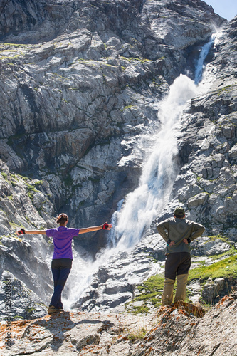 Woman and man hikers are standing on the rock barefoot and enjoys waterfall view. photo