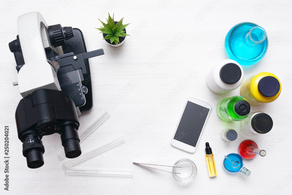 Laboratory table with a microscope, mobile phone and a chemical reagent liquids above. Chemistry or pharmacy background with copy space. Flat lay. Laboratory table with a microscope, mobile phone and a chemical reagent liquids above. Chemistry or pharmacy background with copy space. Flat lay.