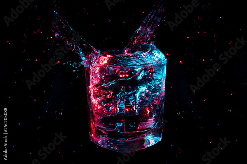 Artistic glowing colorful splash from a rocks glass with isolated droplets on a black background
