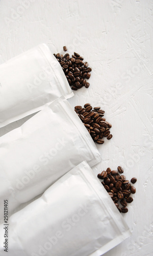 Roasted coffee beans of different varieties poured from three white packs onto the table