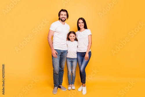Full length body size view portrait of nice sweet lovely attractive cheerful cheery people mom dad hugging pre-teen girl isolated over shine vivid pastel yellow background © deagreez