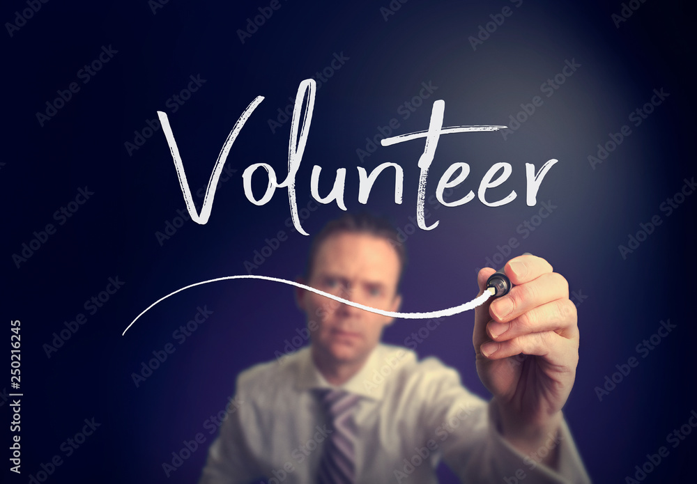 A businessman writing a Volunteer concept with a white pen on a clear screen. A businessman writing a Volunteer concept with a white pen on a clear screen.