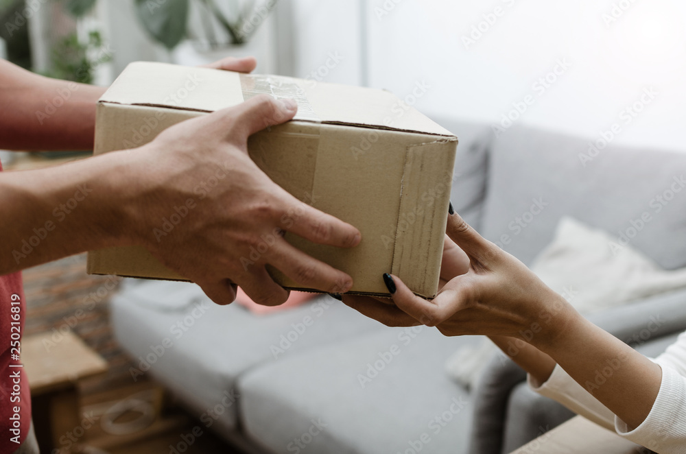 Obraz premium close up hand of home delivery service man in uniform handing parcel boxes to recipient and young customer accepting parcel post box from courier at home, express delivery and online shopping concept