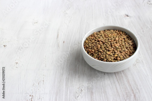 Brown lentils in white bowl on white wooden background