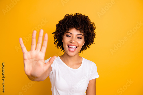 Close up photo beautiful amazed she her dark skin lady glad arms hands five fingers raised show countable uncountable things lesson wearing casual white t-shirt isolated yellow bright background photo