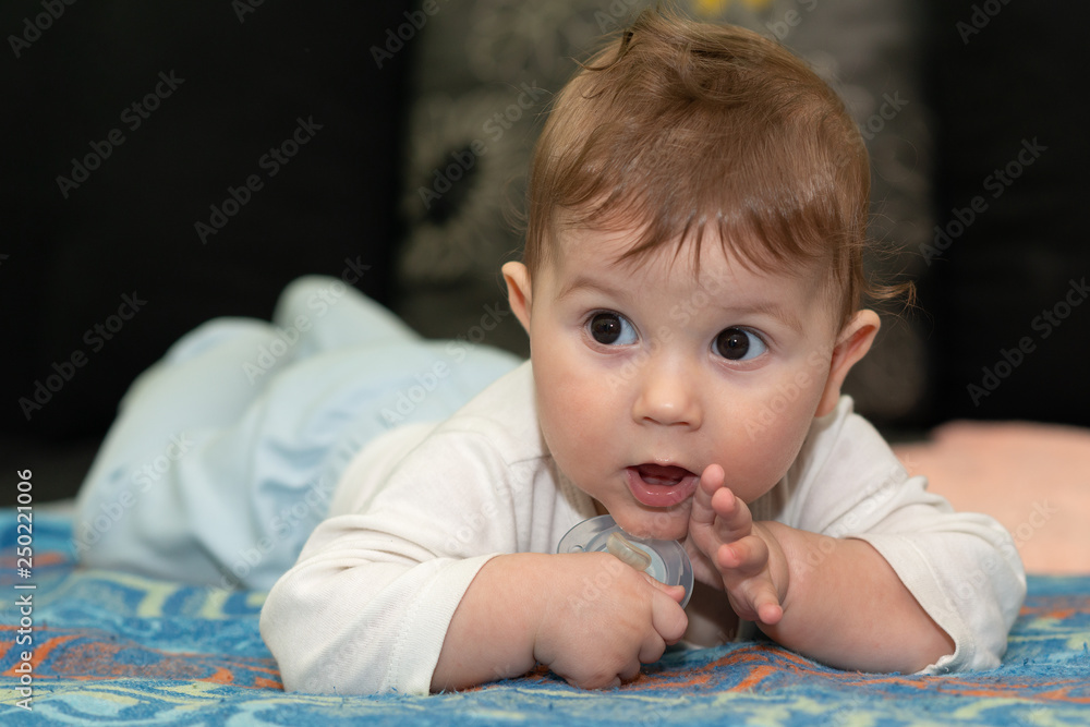 Baby boy is lying on tummy. The baby boy poses and plays with a pacifier. Baby boy is lying on tummy. The baby boy poses and plays with a pacifier.