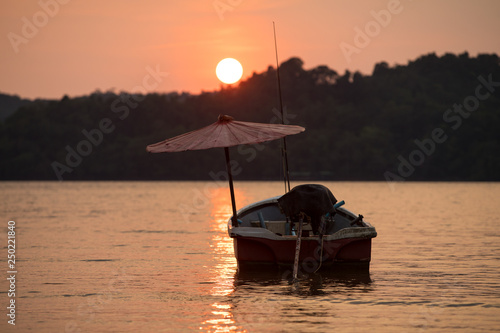 Fishing boat in contra light with umbrella at Golden sunset in calm evening sea