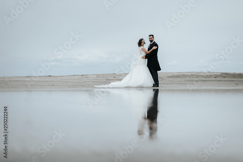 Adorable wedding couple walking along the beach  reflecting in the water. Panoramic view.