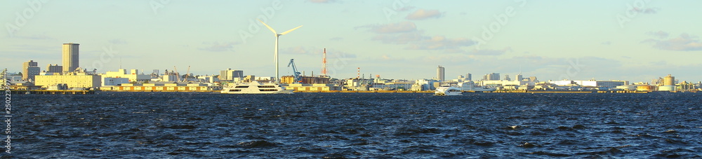 wide panorama view of coastal city's industrial area and deep blue sea water with windmill, ships and warehouses