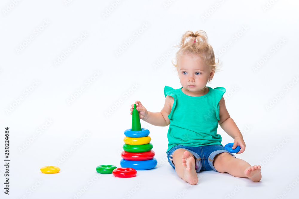 Cute kid blonde girl playing with color pyramid toy isolated on white background. Happy childhood and pre-school development of children Cute kid blonde girl playing with color pyramid toy isolated on white background. Happy childhood and pre-school development of children