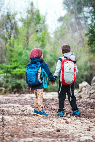 Two boys with backpacks are walking along a forest path. © zhukovvvlad