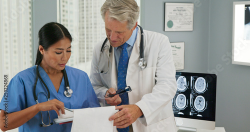 Male and female doctors working together on patient care while standing in hospital office. Surgeon or nurse talking to consulting physician about medical records