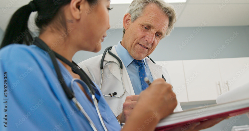 Happy Male and female medical professionals smile while consulting on patient records together. Doctor talking to surgeon or nurse in blue scrubs about treatment options in hospital Happy Male and female medical professionals smile while consulting on patient records together. Doctor talking to surgeon or nurse in blue scrubs about treatment options in hospital