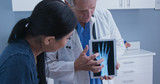 Doctor using tablet computer with x-ray of hand to talk about arthritis with young patient. Senior Caucasian male medical professional with screen demonstrating joint injury to woman