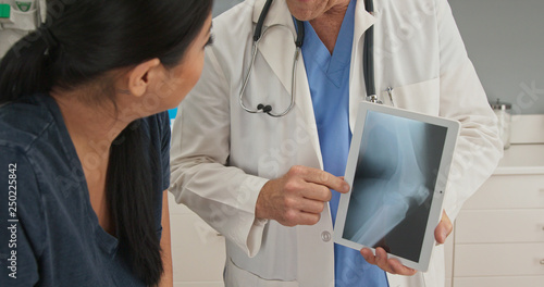 Close up on hands of doctor explaining knee injury while holding tablet computer with x-ray. Patient watching medical professional demonstrate problem with her joints photo