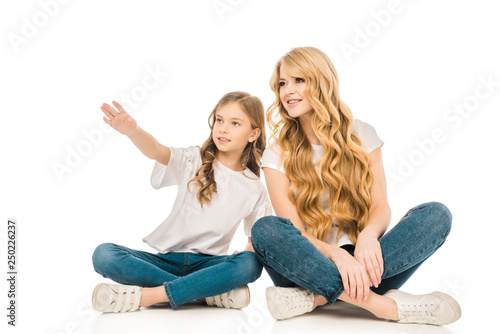 cute child pointing hand while sitting on floor near mother on white background © LIGHTFIELD STUDIOS