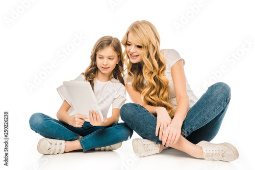 beautiful woman and cute child sitting on floor and using digital tablet on white background