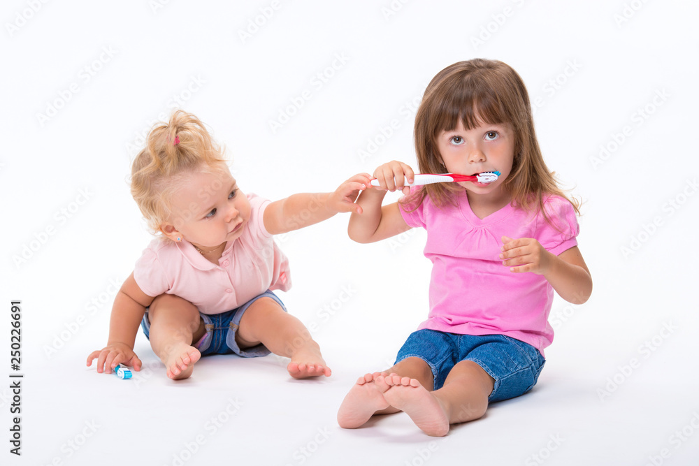 Two girls sisters in pink t-shirt with toothbrushes stand to their full height isolated on white background. Children oral and dental hygiene Two girls sisters in pink t-shirt with toothbrushes stand to their full height isolated on white background. Children oral and dental hygiene