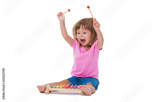 Cute smiling cheerful positive girl 3 years old playing with musical instrument toy xylophone isolated on white background