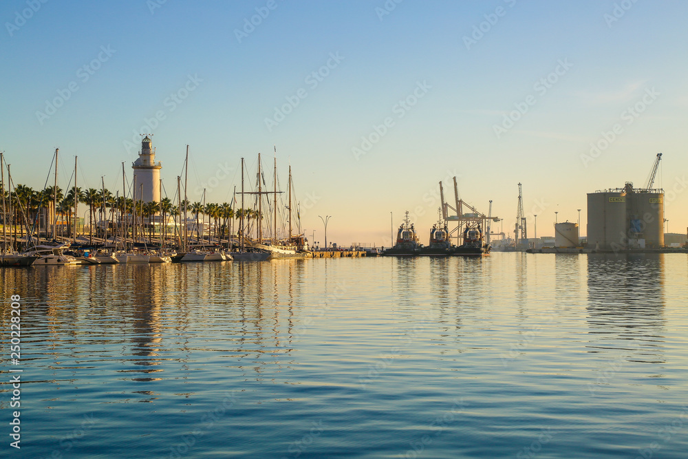 Container port and lighthouse of malaga at sunset with water reflection Container port and lighthouse of malaga at sunset with water reflection