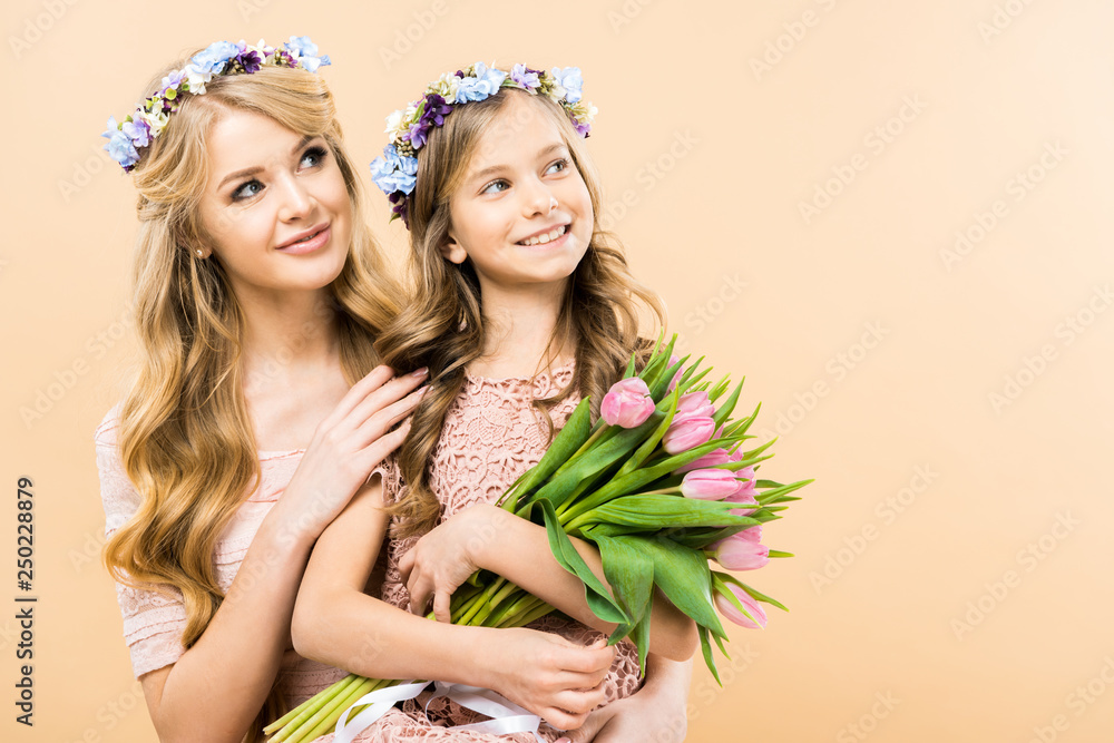 beautiful mother and adorable daughter in floral wreaths looking away and smiling on yellow background beautiful mother and adorable daughter in floral wreaths looking away and smiling on yellow background