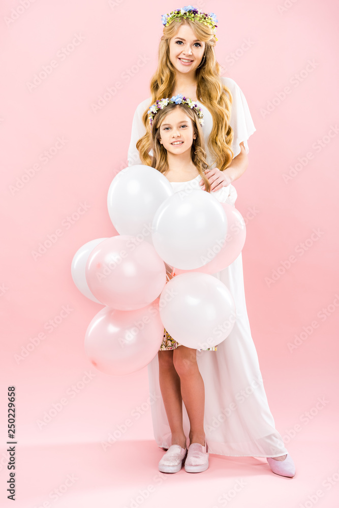 smiling child with festive air balloons standing near happy mother on pink background