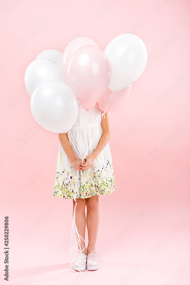 child in delicate white dress hiding behind white and pink air balloons on pink background child in delicate white dress hiding behind white and pink air balloons on pink background