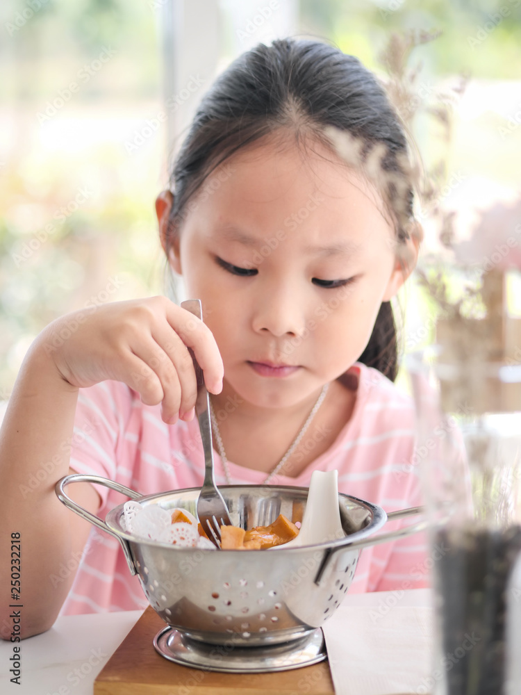 Asian girl eating fried sausages in the aluminium bowl near window at home. Asian girl eating fried sausages in the aluminium bowl near window at home.