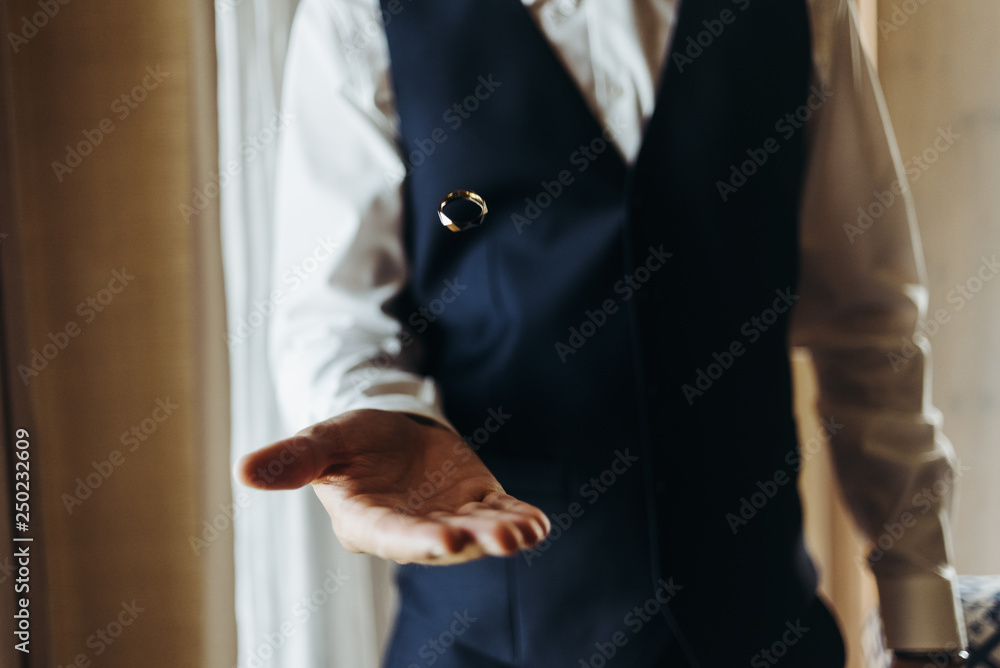 Groom holds wedding ring standing before the window in a hotel room Groom holds wedding ring standing before the window in a hotel room