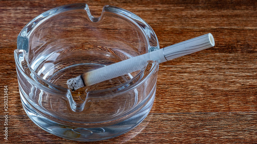glass ashtray with a cigarette from which there is smoke