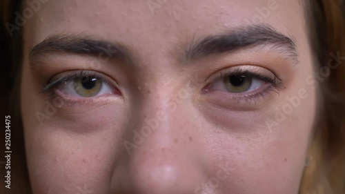 Closeup portrait of young beautiful caucasian female face with green eyes staring straight at camera with tired look