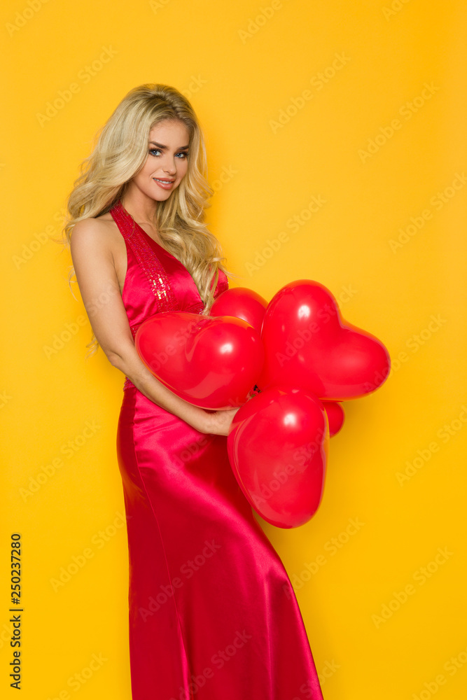 Smiling Beautiful Woman In Elegant Red Dress Is Posing With Heart Shaped Balloons Smiling Beautiful Woman In Elegant Red Dress Is Posing With Heart Shaped Balloons
