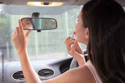 Attractive young woman applying lipstick looking at mirror in car..Girl adjusts her makeup putting lipstick while sitting at the wheel of a car. 