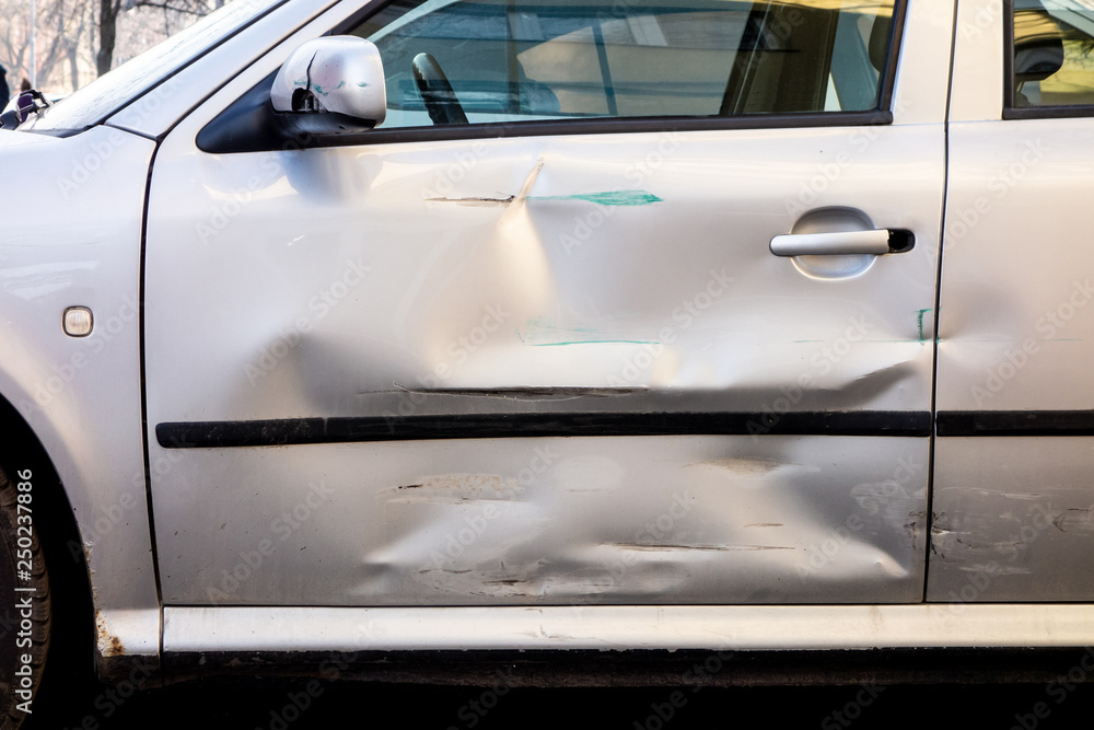 Damaged side door on a silver car after a small traffic accident Damaged side door on a silver car after a small traffic accident