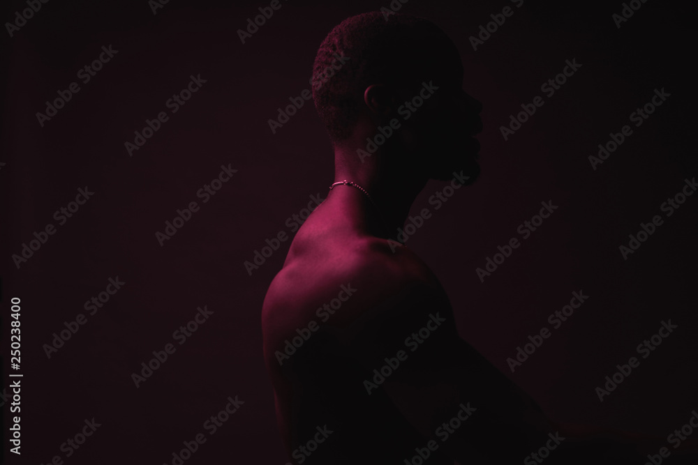 Red and blue lighted portrait of young and sexy muscular shirtless man with neck chain.