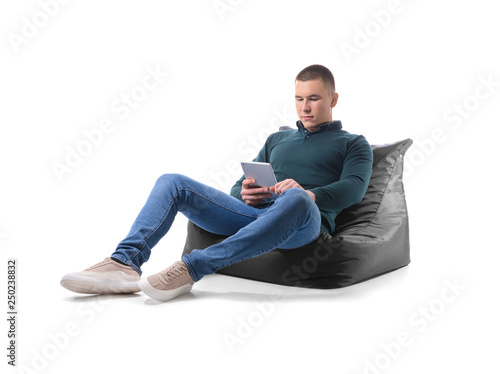 Young man with tablet computer relaxing on beanbag against white background