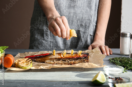 Woman squeezing lemon juice onto tasty mackerel fish on table