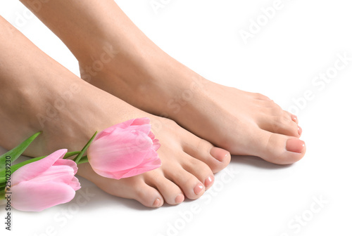 Legs of young woman with beautiful pedicure and flowers on white background