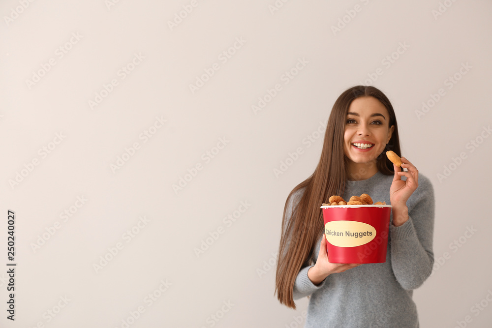 Young woman with bucket of tasty nuggets on light background Young woman with bucket of tasty nuggets on light background