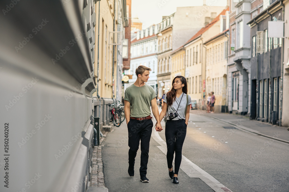 Young couple holding hands while walking along a city sidewalk
