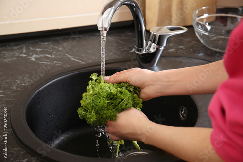 Young woman washing fresh parsley in kitchen sink