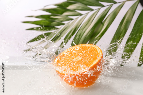 Ripe cut orange with water splash and tropical leaf on white background