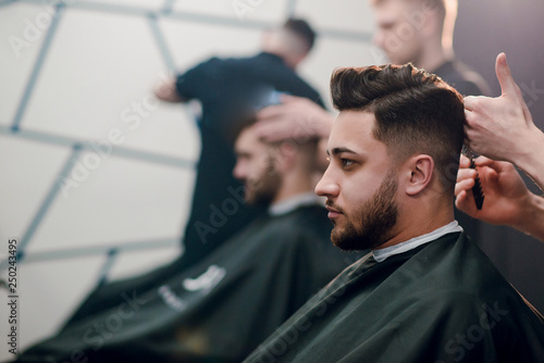 Obraz na płótnie Young handsome brunette man getting haircut by hairdresser in barbershop