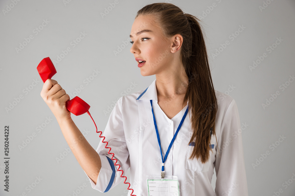 Beautiful young woman cosmetologist doctor isolated over grey wall background talking by telephone. Beautiful young woman cosmetologist doctor isolated over grey wall background talking by telephone.
